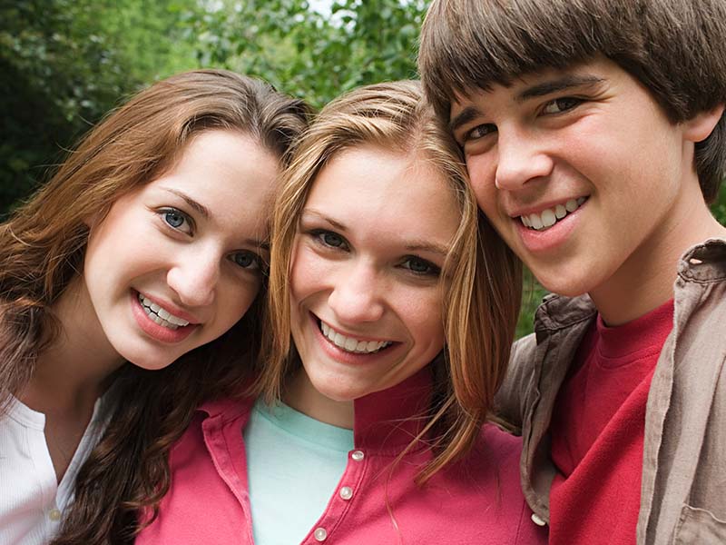Three teenagers smiling together outdoors