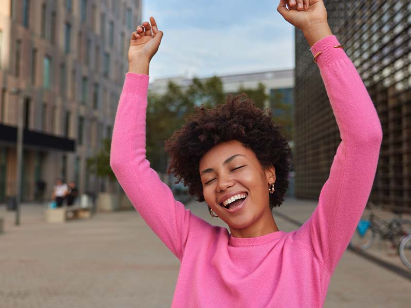 Woman in a pink sweater smiling with her arms raised